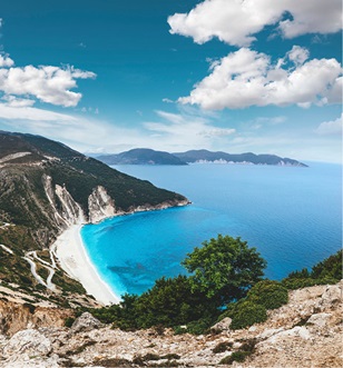 aerial view of a beach cove surrounded by mountains and cliff faces with vibrant blue water
