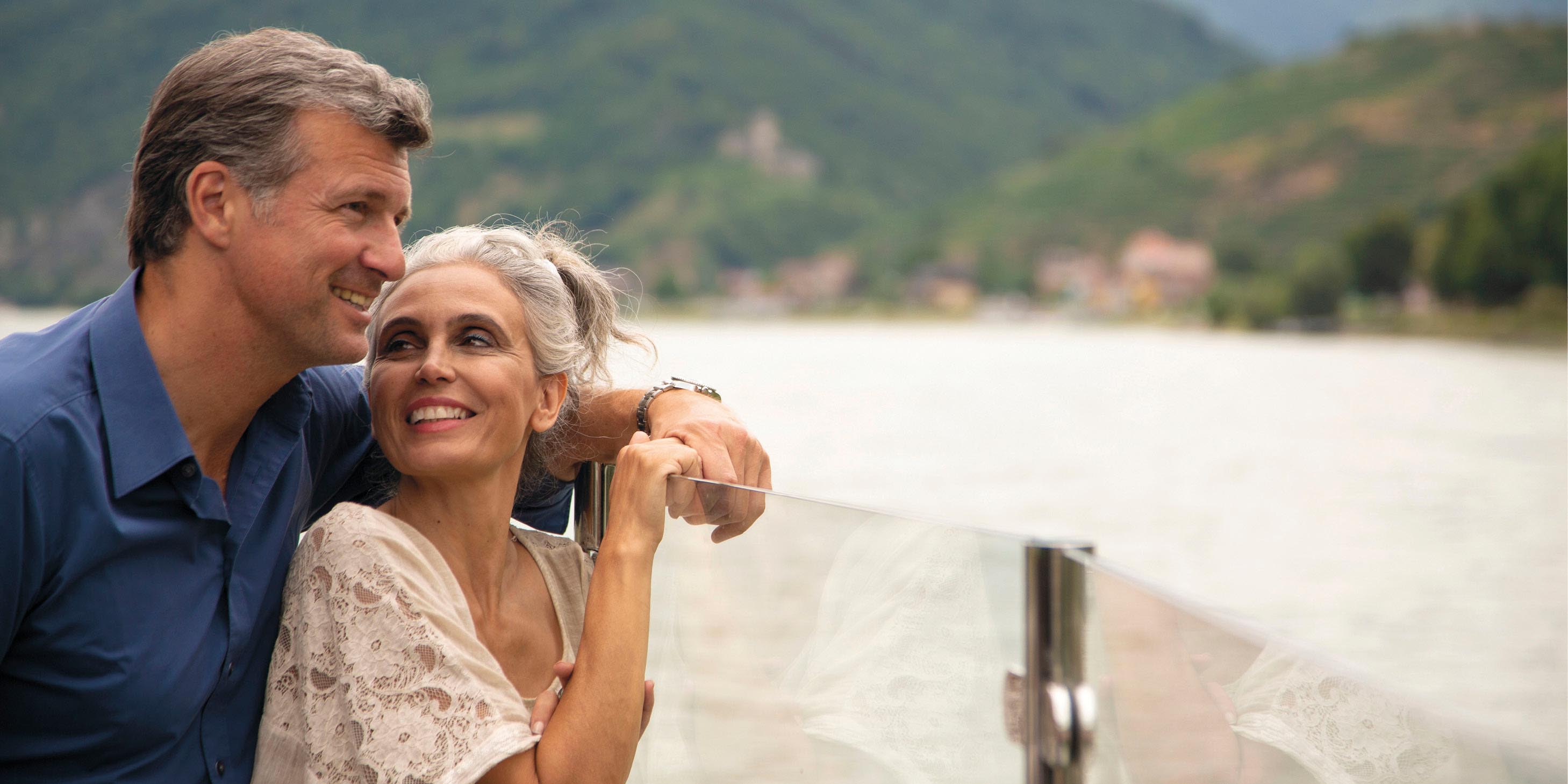 A man and a woman admiring the view from the top deck of a cruise ship sailing down a river