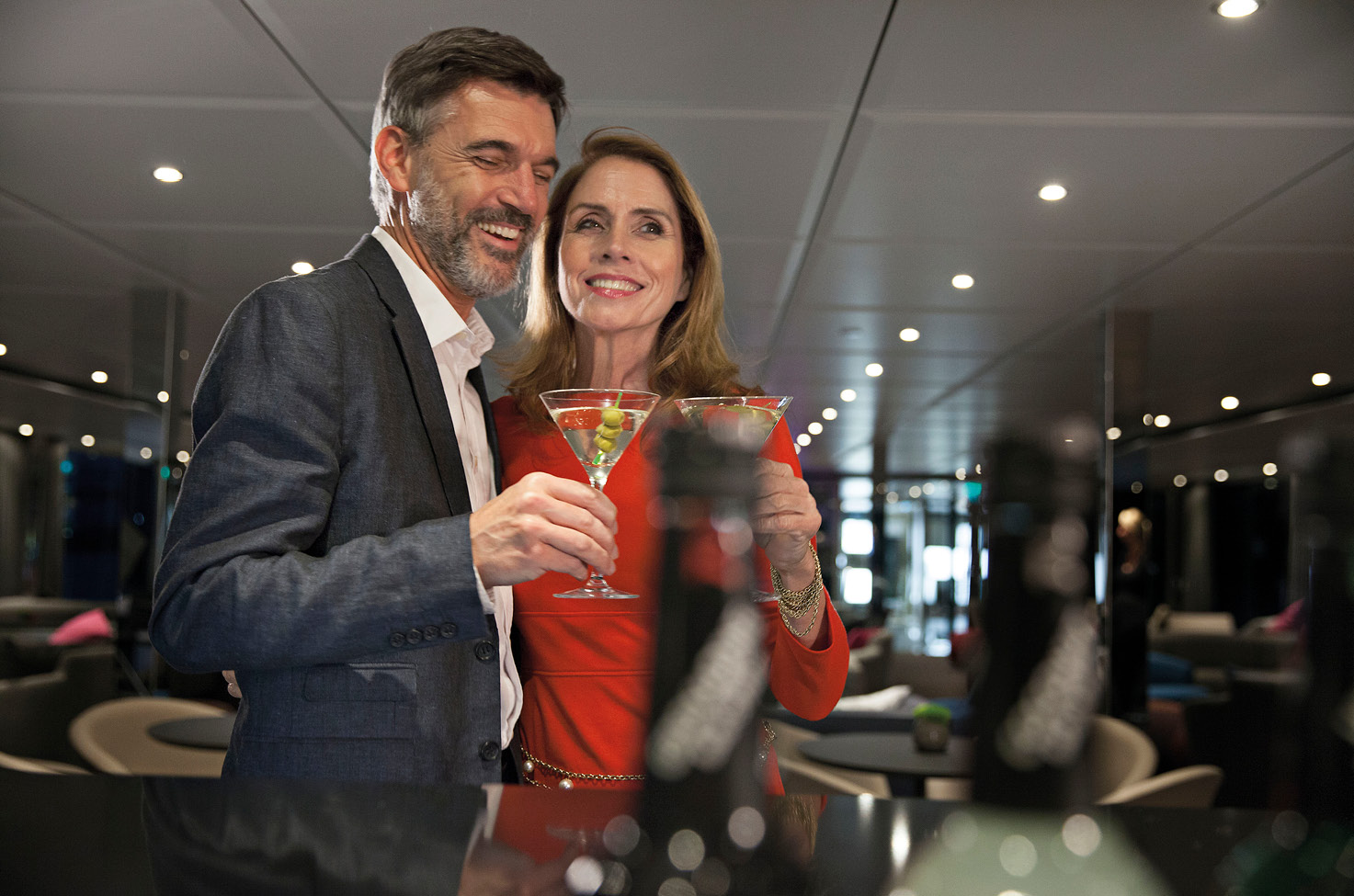Smartly dressed man and woman smiling as they drink martini cocktails
