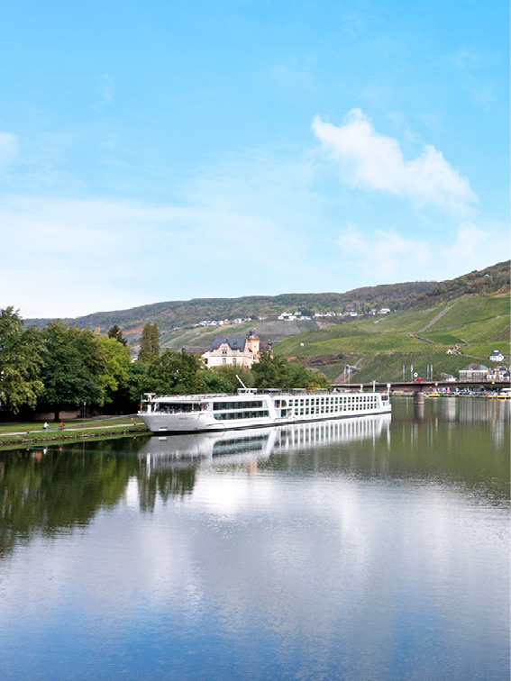 Luxury river ship docked in Bernkastel, Germany, with the landscape reflected in the water’s surface. 