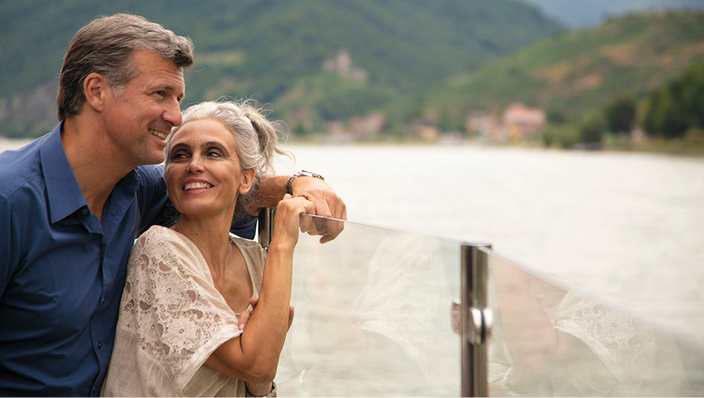 A man and a woman admiring the view from the top deck of a cruise ship sailing down a river