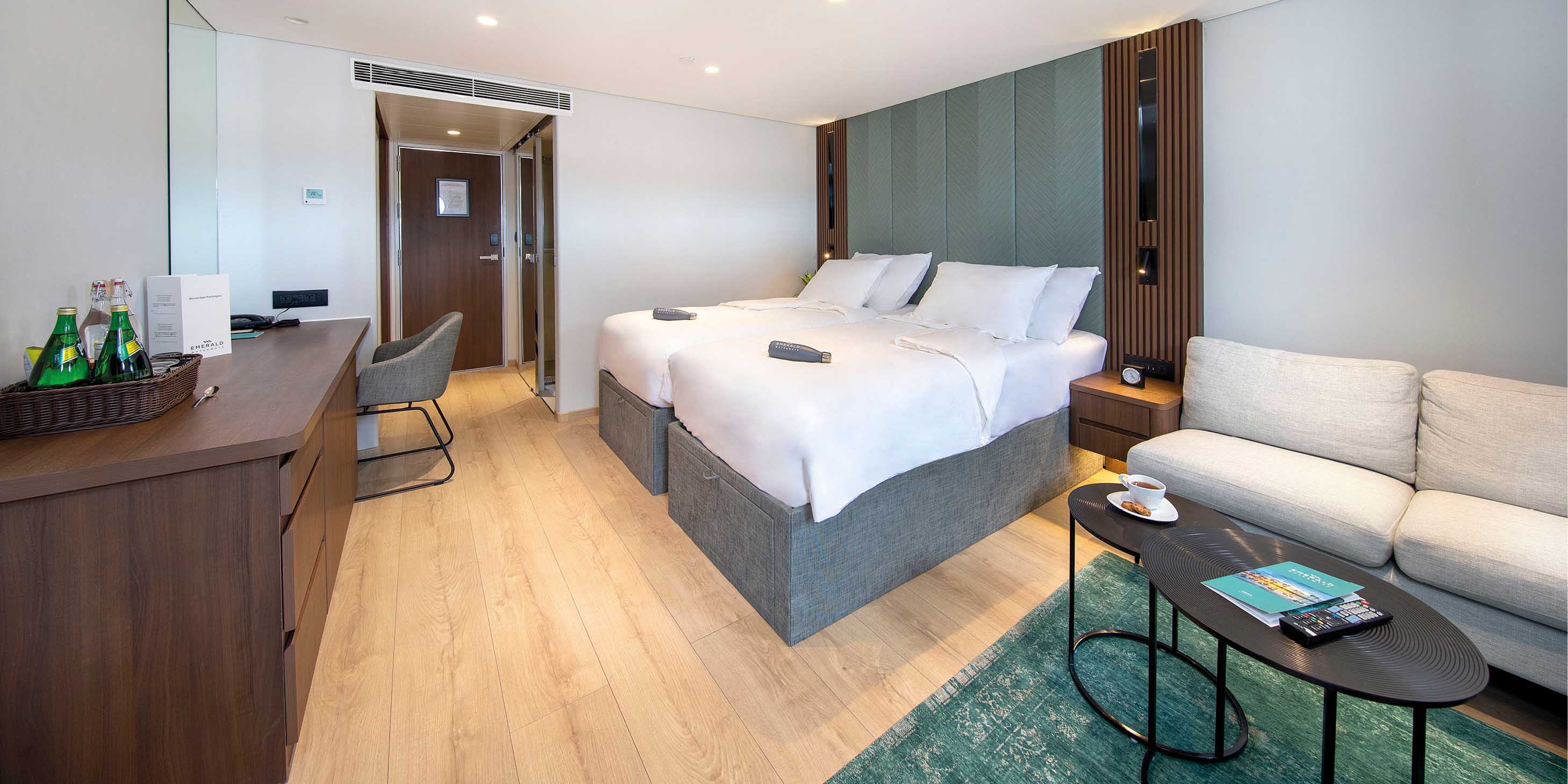 Spacious cruise ship accommodation, with twin beds, desk and chair, plus a lounge area with sofa and coffee table