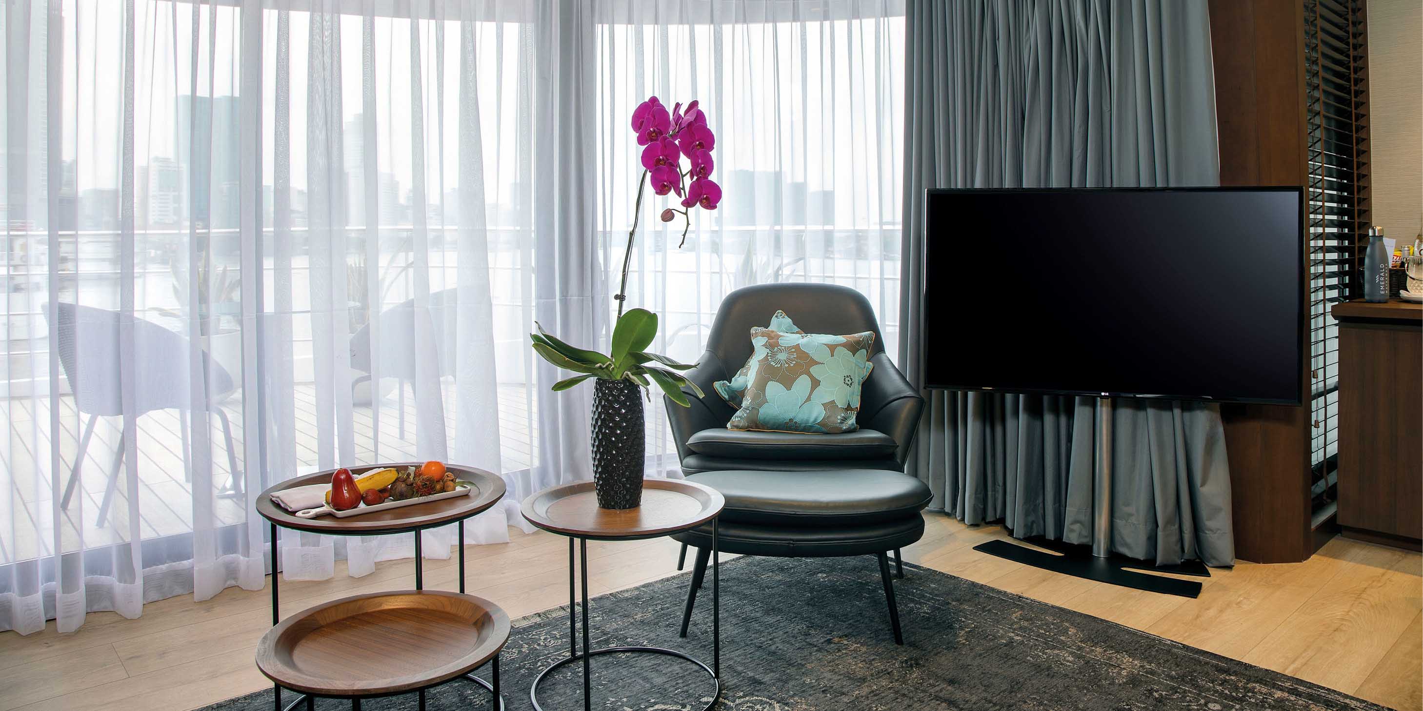 Close-up of TV, chair, footstool, and tables in lounge area, with private terrace visible through the curtain window