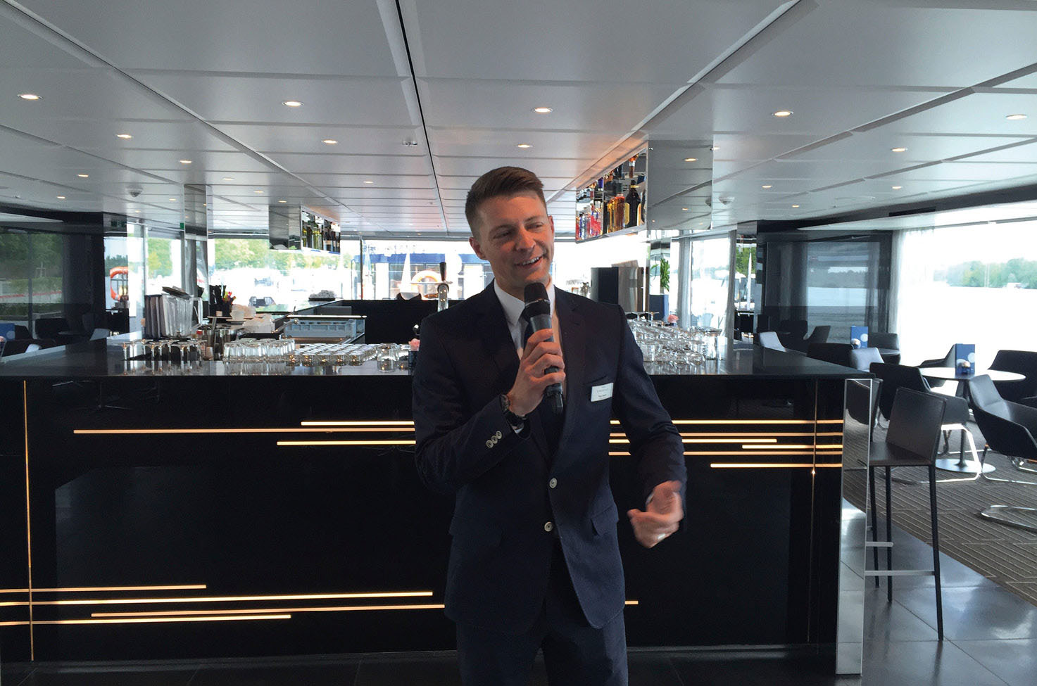 Man standing in front of a bar, holding a microphone and giving a speech